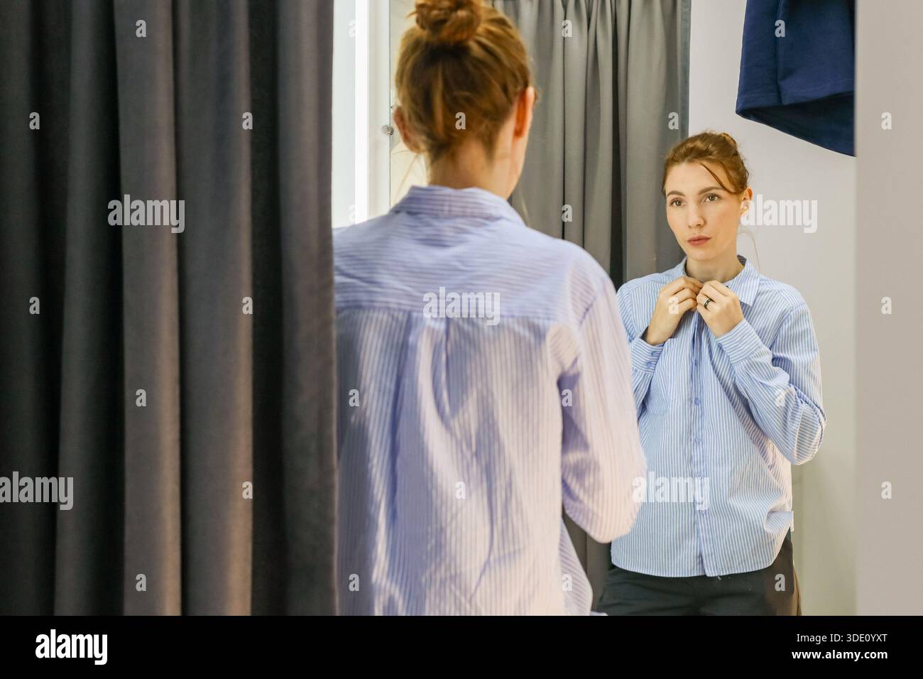 La persona in camicetta a righe esamina l'abbigliamento a specchio della cabina di montaggio con tende e grucce Foto Stock