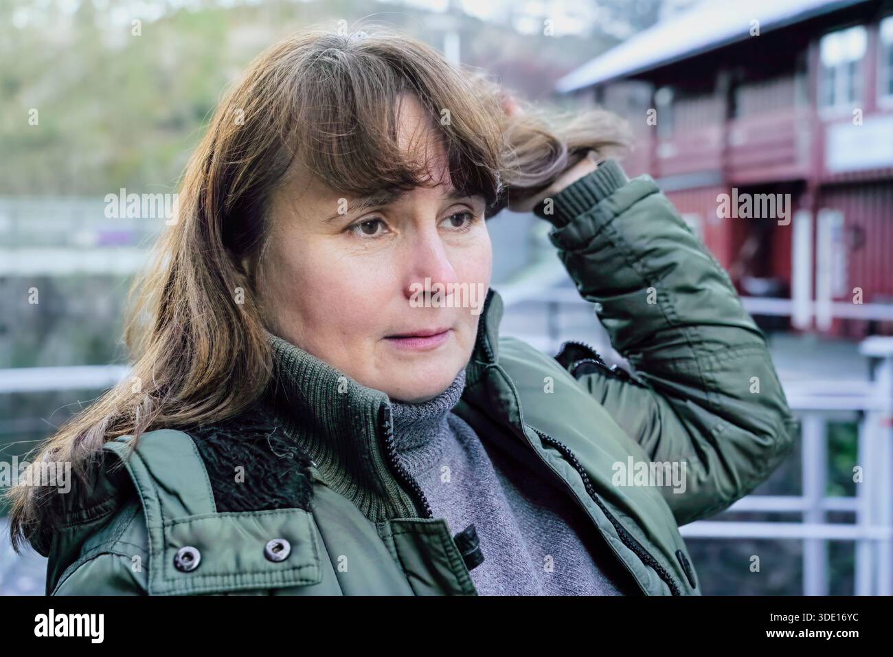 Consapevole consapevolezza di sé, espressa come una donna adulta tocca i capelli all'aperto, facendo una pausa durante una passeggiata per riconnettersi con se stessa, riflettendo una vita lenta, Foto Stock