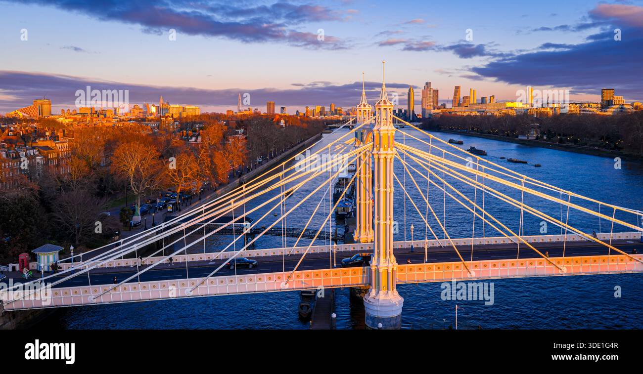 Vista panoramica dell'Albert Bridge sul fiume Tamigi all'ora d'oro, che collega Chelsea e Battersea mentre lo skyline di Londra si illumina; per i viaggi, i trasporti, Re Foto Stock