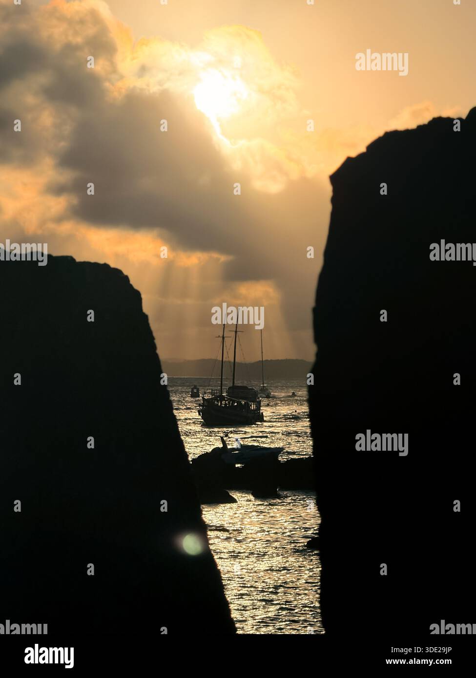 Tramonto dell'ora d'oro con raggi del sole che si infrangono attraverso le nuvole sull'oceano. Incorniciato dal muro di pietra del forte Morro de São Paulo a Bahia, Brasile - Immagine stock catturata con smartphone