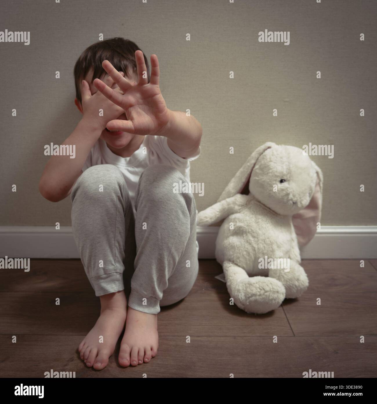 Un bambino spaventato siede sul pavimento coprendo il viso, simboleggiando la paura, il trauma e l'impatto emotivo degli abusi domestici a casa. Foto Stock
