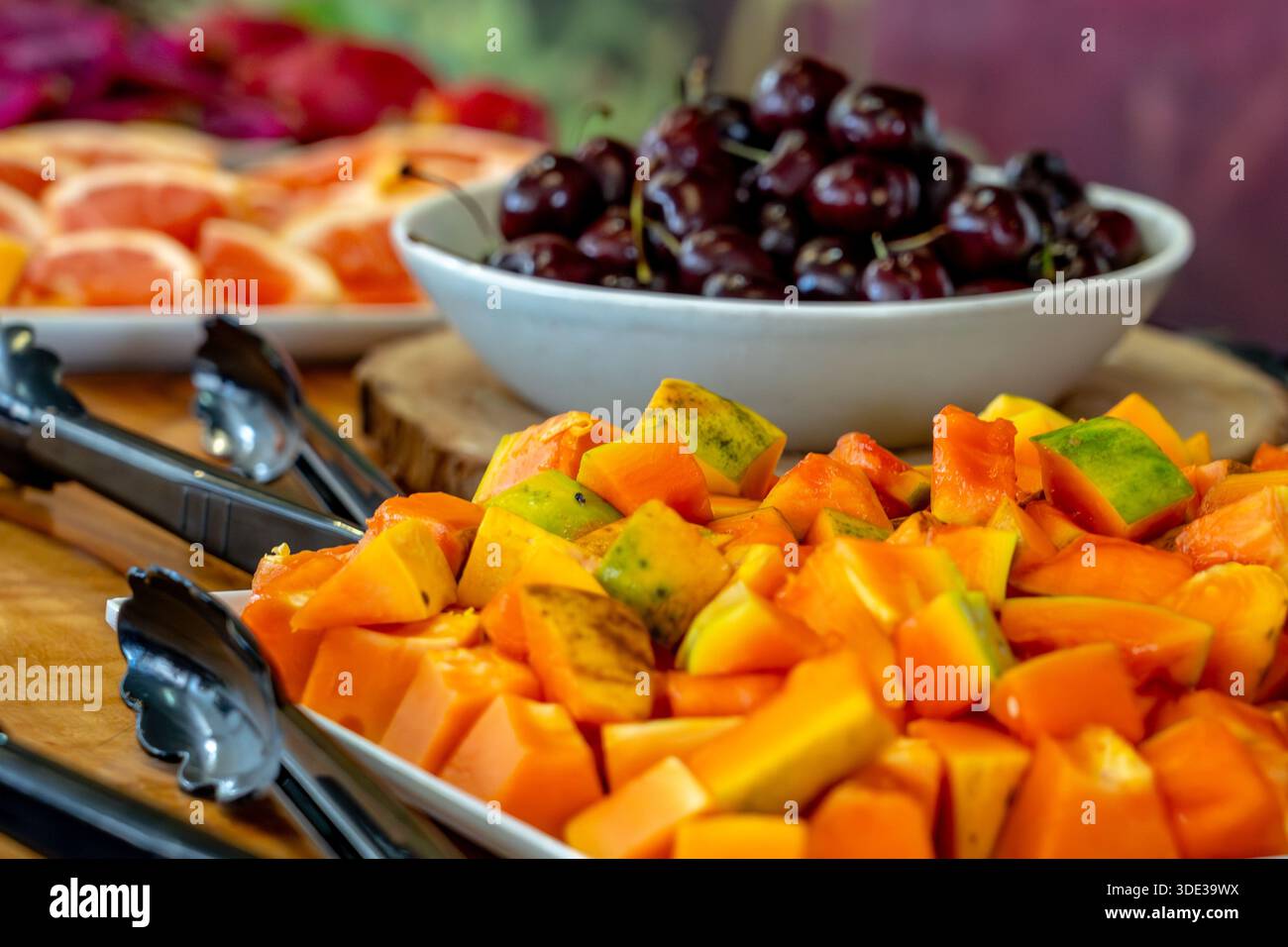 Papaya fresca matura tagliata su un piatto con ciliegie sullo sfondo Foto Stock