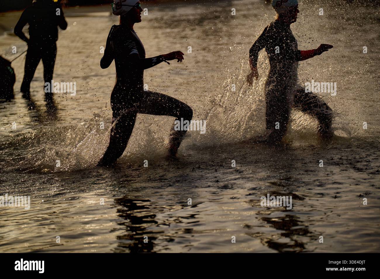 Due atleti corrono in acque poco profonde durante una gara di nuoto che si tiene la mattina presto. Il sole proietta un caldo bagliore sulla scena. Foto Stock