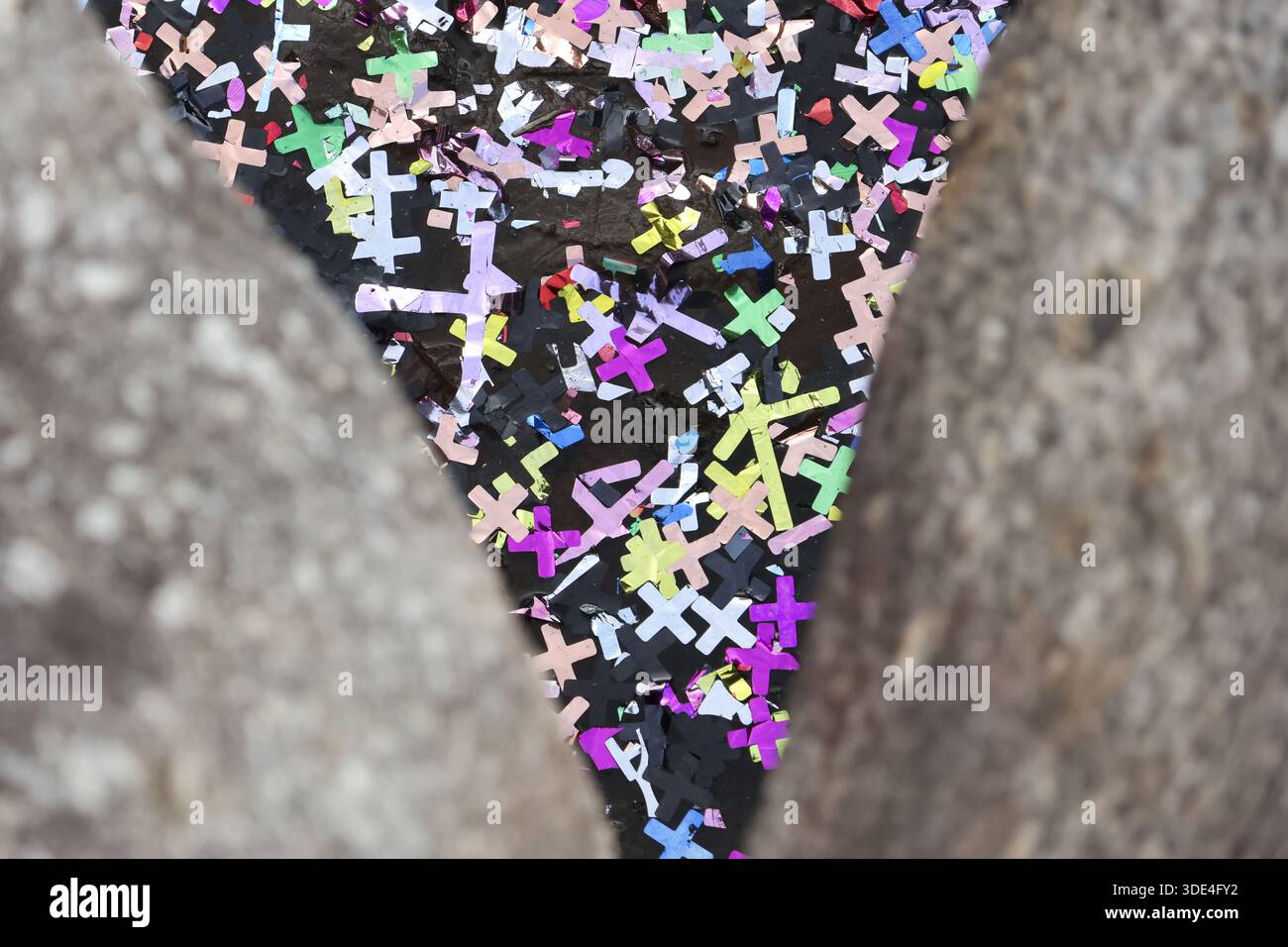 Fessura triangolare colorata piena di coriandoli a croce che mostrano uno spirito festoso tra bordi in cemento grezzo di pietra grigia Foto Stock