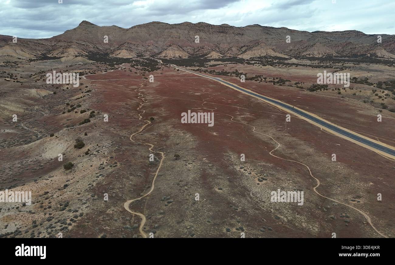 Vista aerea di un terreno aspro e arido si estende verso le Book Cliffs, un nastro di strada che taglia attraverso il paesaggio color ruggine sotto una vasta nuvola Foto Stock