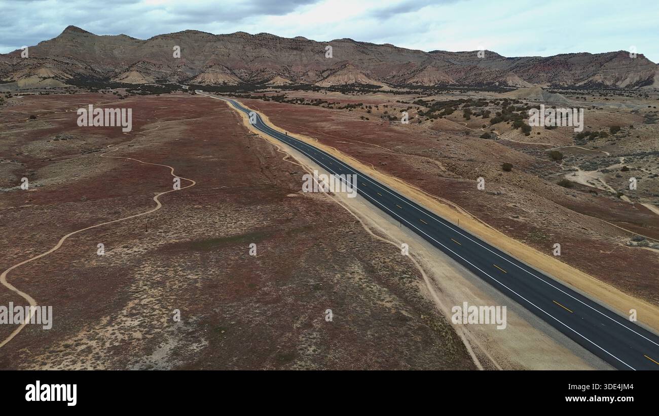 Veduta aerea di un nastro di asfalto che taglia attraverso il paesaggio arido, contrastando con le aspre scogliere del Libro che incombono in lontananza, Fruita, Colora Foto Stock