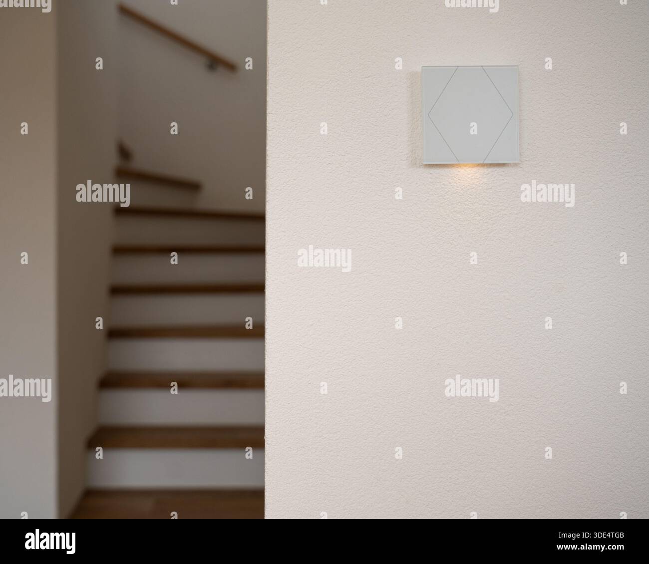 Corridoio moderno con lampada da parete luminosa accanto a una scala in legno. Luce calda e ombre morbide creano un'atmosfera accogliente e accogliente, ideale per gli interni Foto Stock
