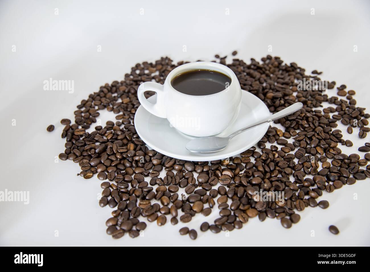Una tazza di caffè posta su una superficie con chicchi di caffè sparsi intorno. La composizione mette in risalto le ricche tonalità di marrone e l'aroma di pasta fresca Foto Stock