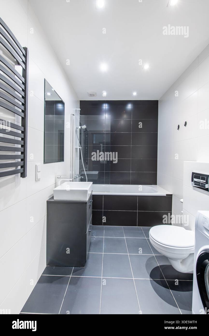 Bagno moderno e luminoso con elegante arredo bianco e nero, vasca, WC e lavatrice Foto Stock