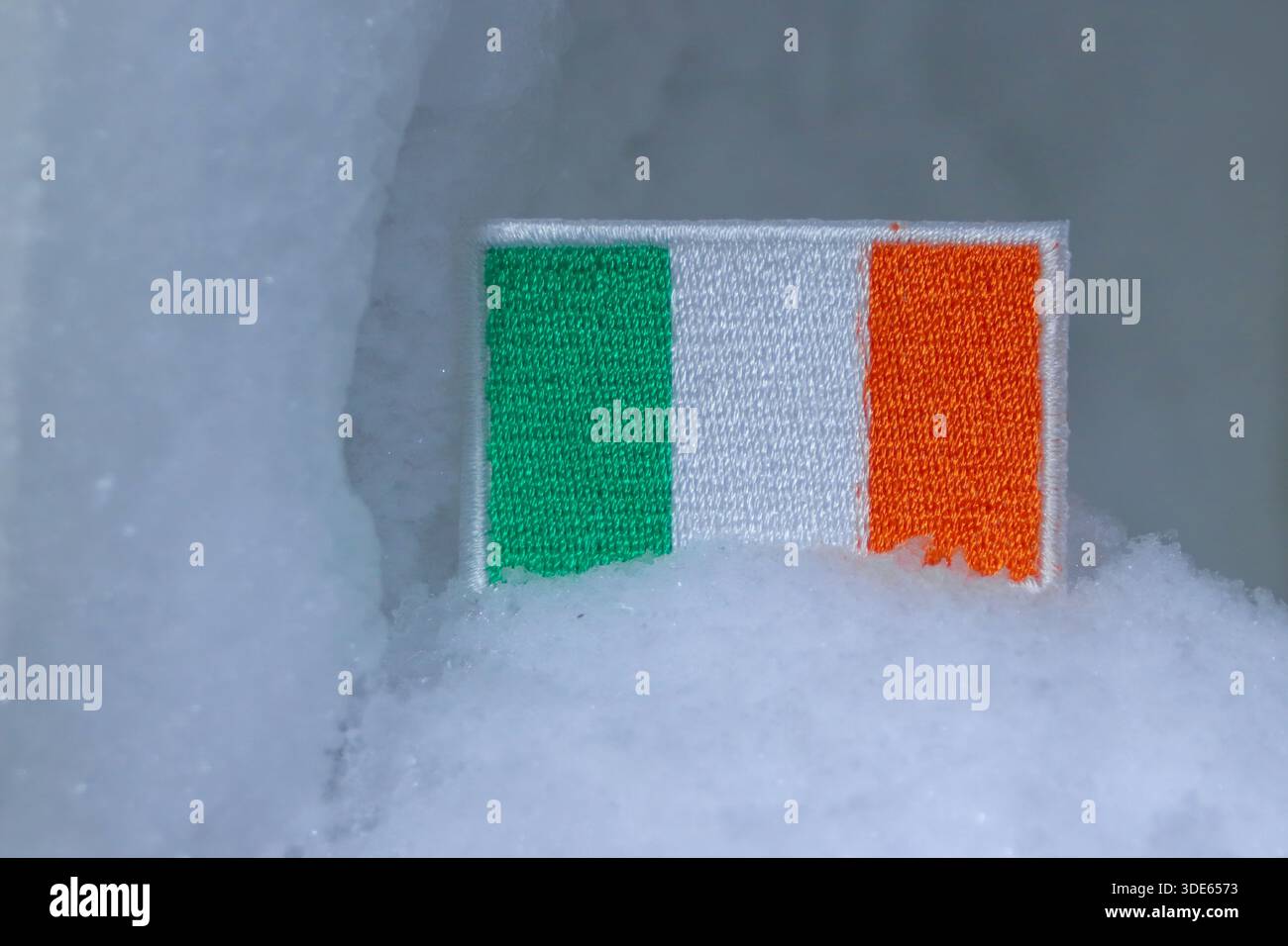 Bandiera irlandese in un ambiente innevato. Simbolo delle condizioni meteorologiche in Irlanda, delle tempeste invernali e della resilienza del paese in caso di gelo freddo. Foto Stock