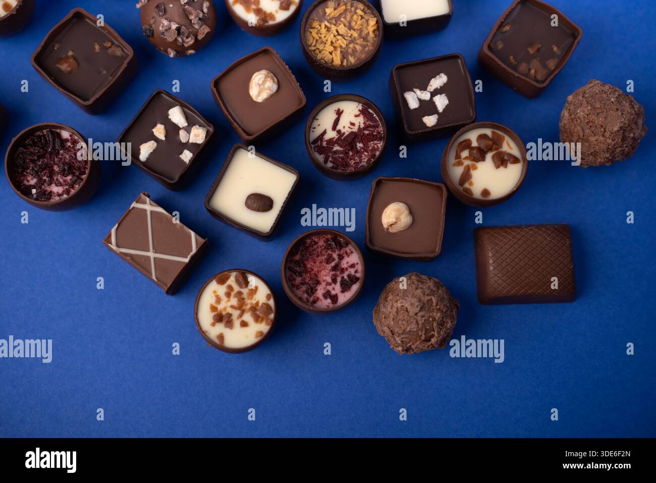 primo piano di cioccolatini e tartufi gourmet assortiti disposti su un vivace sfondo blu, che mostrano forme diverse, ripieni cremosi, noci e. Foto Stock