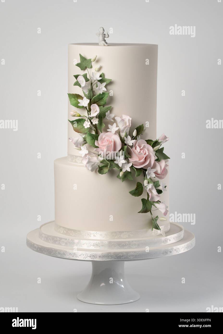 Elegante torta nuziale a due piani con un livello superiore extra alto, decorata con rose rosa in pasta di zucchero lavorata a mano, fiori di gelsomino bianco e foglie verdi Foto Stock