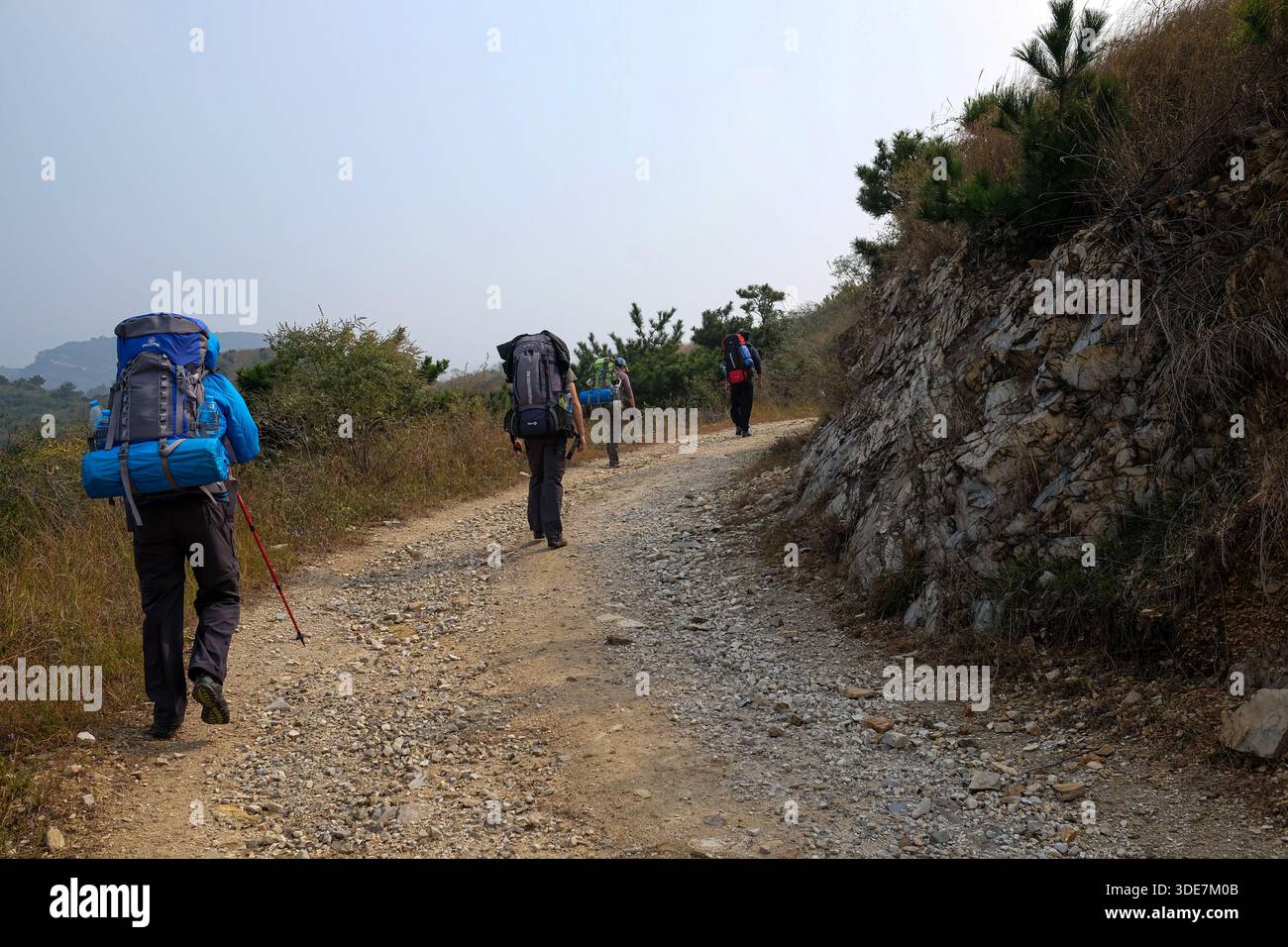 WUHAN, CINA - 31 OTTOBRE 2014: Vista posteriore degli escursionisti con grandi zaini che navigano su terreni diversi. Le immagini mostrano il trekking su sentieri rocciosi di ghiaia, Foto Stock