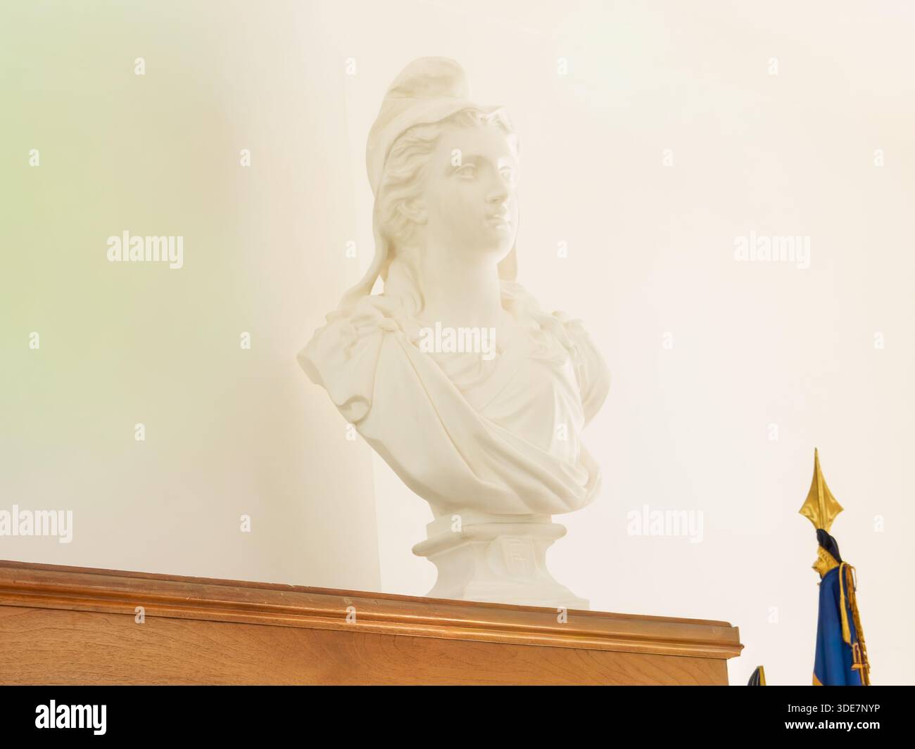 Busto classico in marmo bianco di una figura femminile drappeggiata ispirata all'antica arte greca e romana, esposto all'interno su un morbido sfondo minimalista. Foto Stock