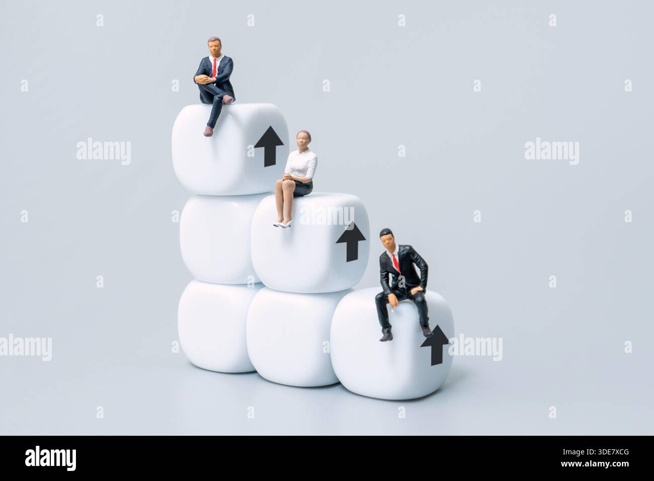 Uomini d'affari in miniatura su blocchi impilati con frecce rivolte verso l'alto. Scala aziendale, crescita, avanzamento di carriera, concetto di gerarchia aziendale. Foto Stock
