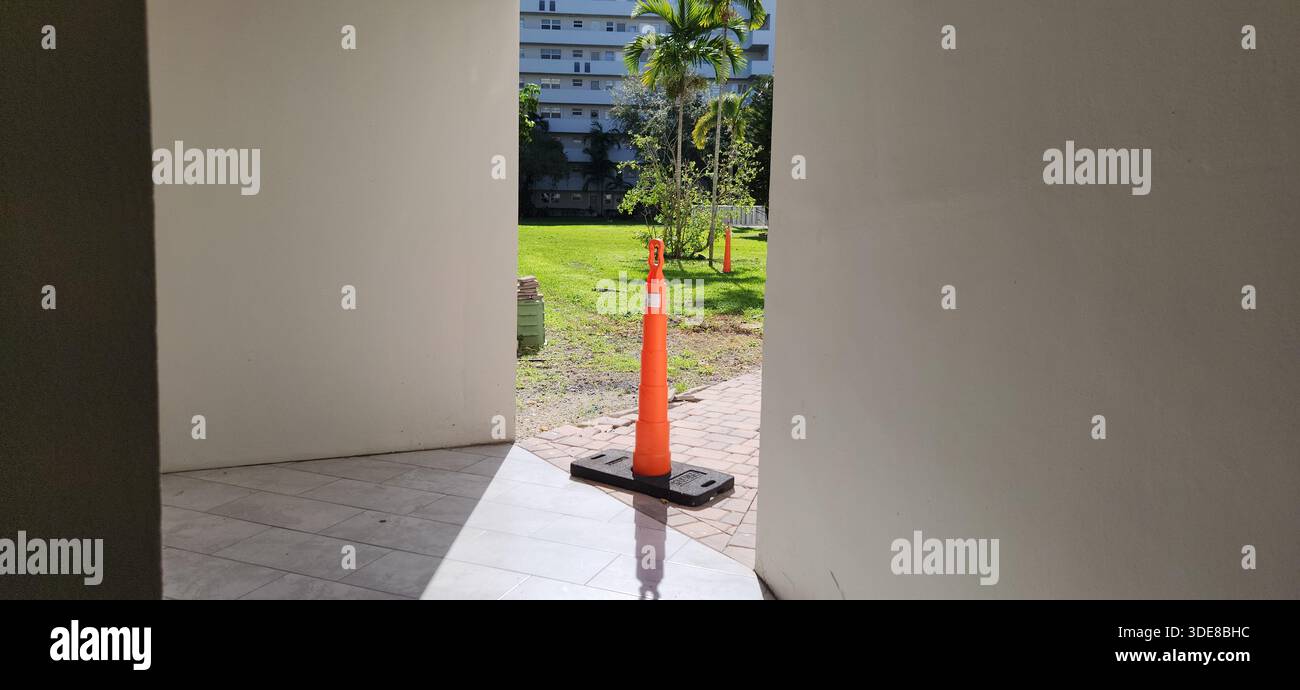 Un cono stradale arancione alto si trova all'uscita di un edificio, segnalando un'area limitata o pericolosa. Spesso utilizzato durante lavori stradali e lavori di costruzione Foto Stock