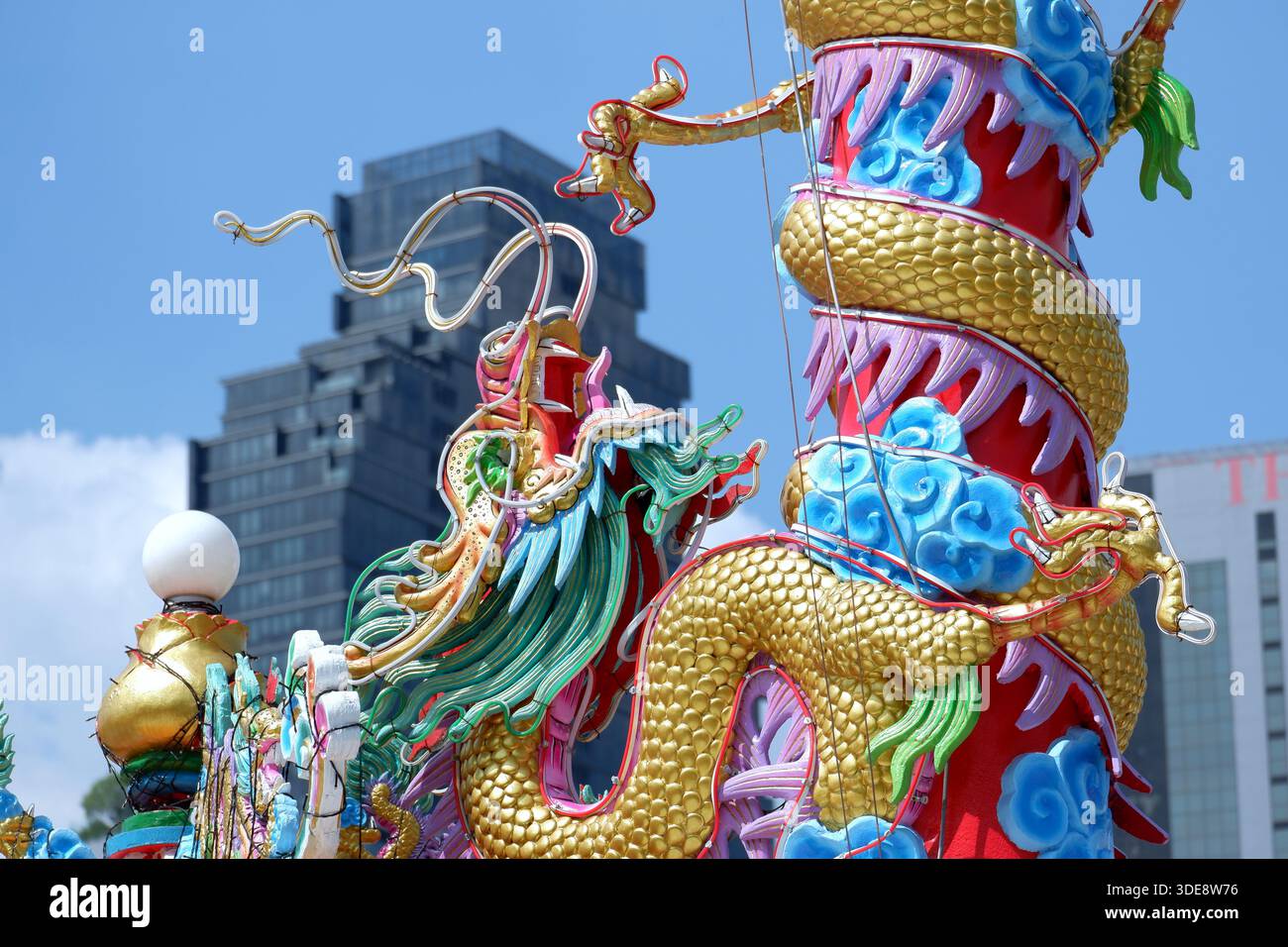Una vista ravvicinata mostra una testa di drago su un palo cerimoniale contro il cielo azzurro del cimitero di Teochew. Sullo sfondo appare un moderno grattacielo di Bangkok. Foto Stock