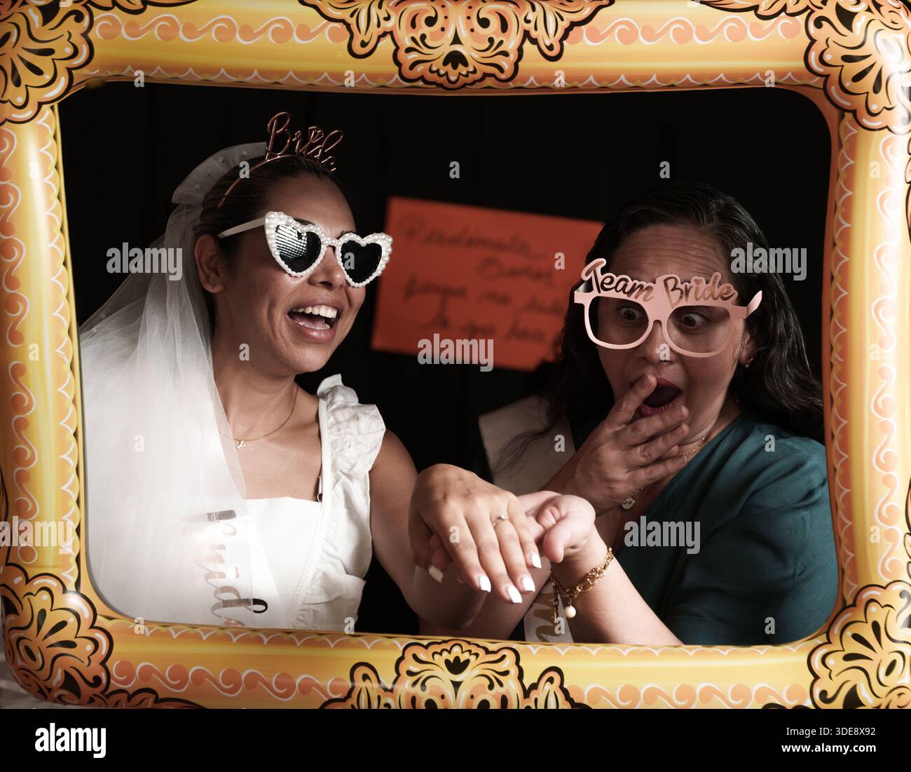 Una donna che indossa un vestito bianco e occhiali da sole sta posato per una foto. Una donna con una camicia blu è in piedi dietro di lei Foto Stock