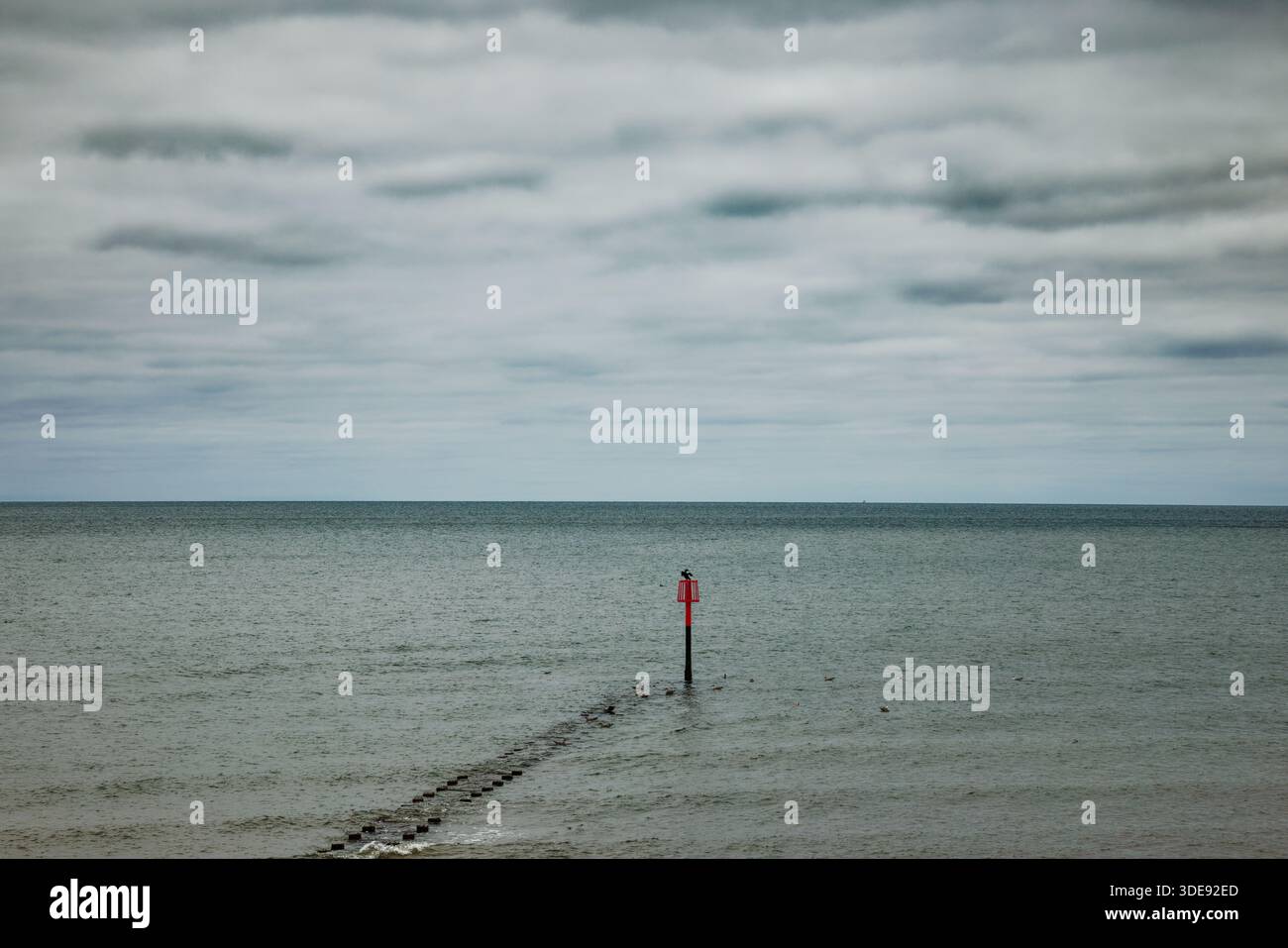 Un pennarello alla fine di un groyne fornisce una macchia di colore in una scena grigia di mare e cielo, Bridlington, East Yorkshire, Inghilterra. Foto Stock