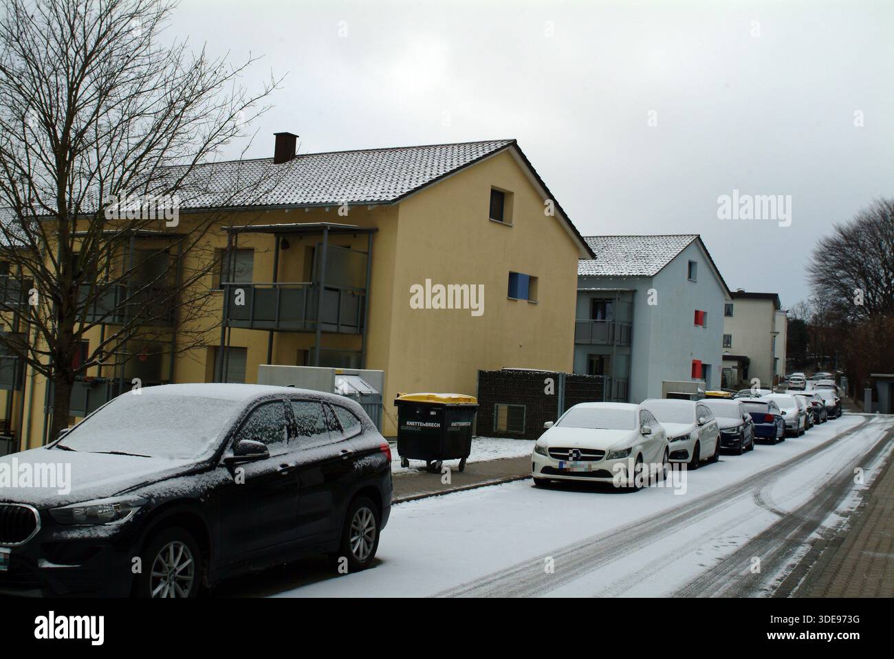Vicolo di periferia ghiacciato fiancheggiato da auto e cestini, tetti spolverati di neve, atmosfera tranquilla all'alba, marciapiedi salati e freddo quiete Keukenhof, Olanda Apr Foto Stock