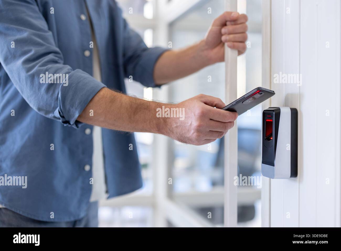 Persona che tiene uno smartphone vicino a un lettore biometrico, accede a un'area protetta, rappresenta i moderni sistemi di sicurezza e l'autenticazione senza contatto per l'ingresso in un edificio Foto Stock