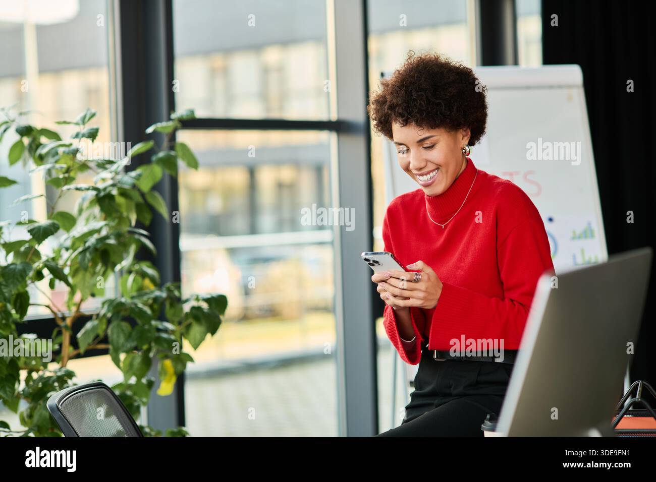 Una giovane manager afroamericana sorride mentre controlla i suoi messaggi in un ufficio elegante. Foto Stock