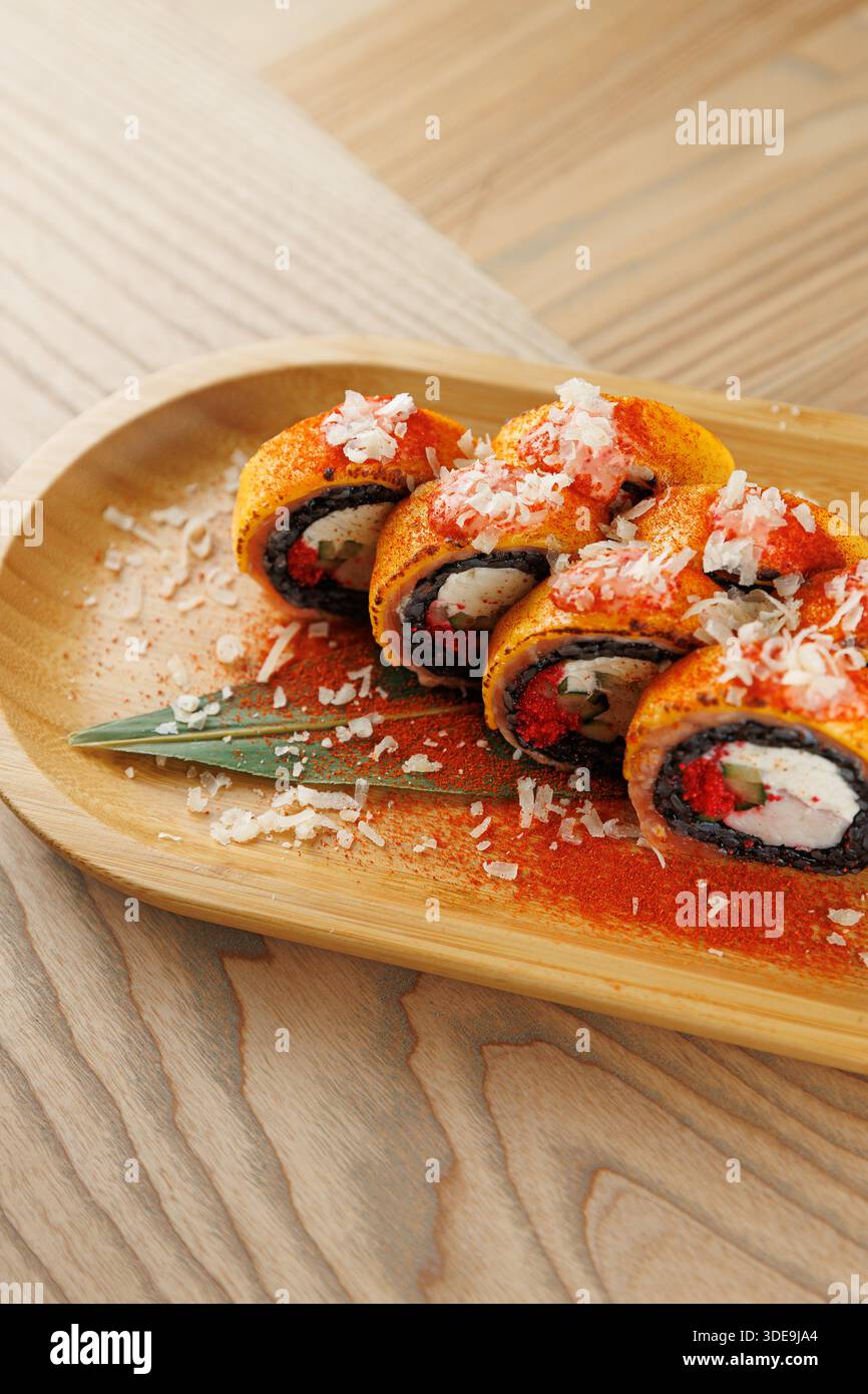 I colorati sushi roll sono disposti su un piatto di legno. I panini contengono ingredienti come riso, verdure e pesce ricoperti di trucioli e spezie. Foto Stock