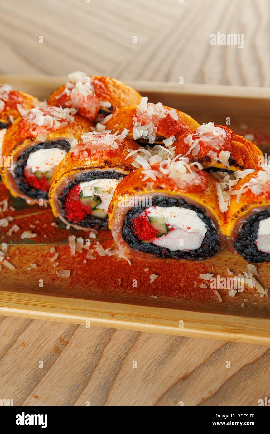 Panini di sushi ripieni di formaggio spalmabile, verdure e conditi con pesce grattugiato e spezie sono presentati su un piatto di legno al tavolo di un ristorante. Foto Stock