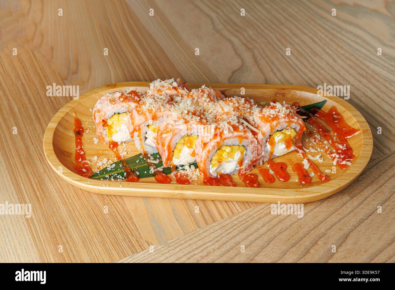 Il piatto di sushi presenta diversi panini conditi con gamberi e guarniti con salsa, serviti su un vassoio di legno in un ambiente rilassato. Foto Stock
