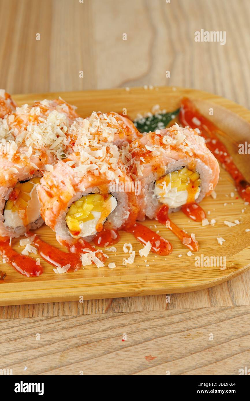 I sushi Rolls sono serviti su un piatto di legno, caratterizzato da strati di pesce e ripieni, conditi con salsa piccante e scaglie croccanti per un pasto piacevole. Foto Stock