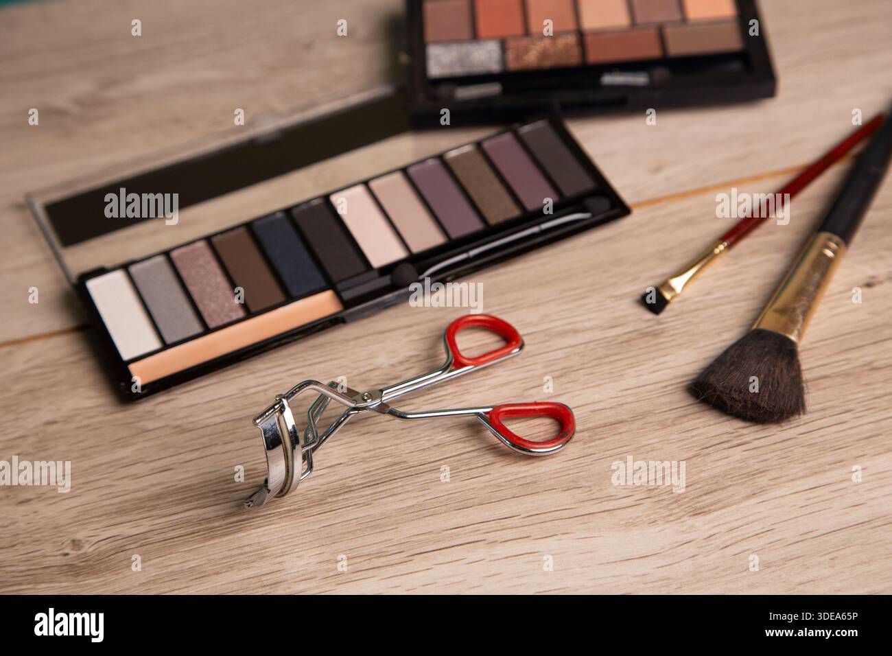 Ci sono degli attrezzi per il trucco su un tavolo di legno. Sono presenti una tavolozza con vari colori, un arricciacapelli mascara, un pennello e uno strumento per la miscelazione del trucco. Foto Stock