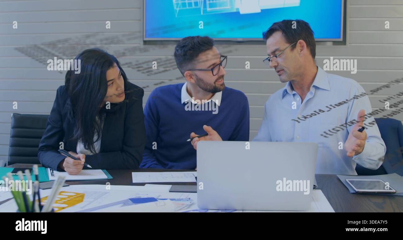 Discutere dei colleghi nella sala riunioni, indossare una camicia, un maglione blu navy, un blazer, rivedere i piani del computer portatile Foto Stock