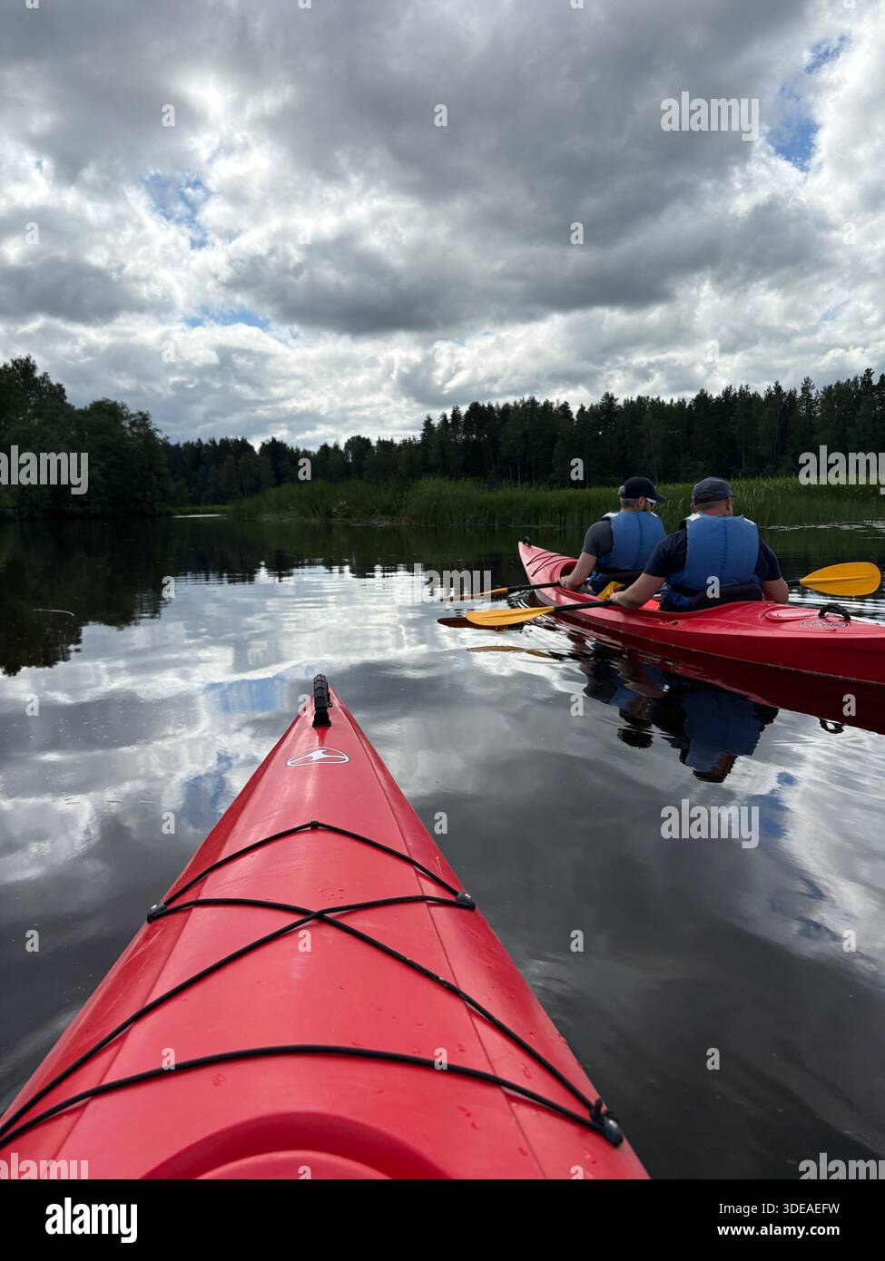 I kayak pagaiano sul tranquillo lago della foresta sotto il cielo nuvoloso, visto dalla terza prospettiva del kayak - Immagine stock catturata con smartphone