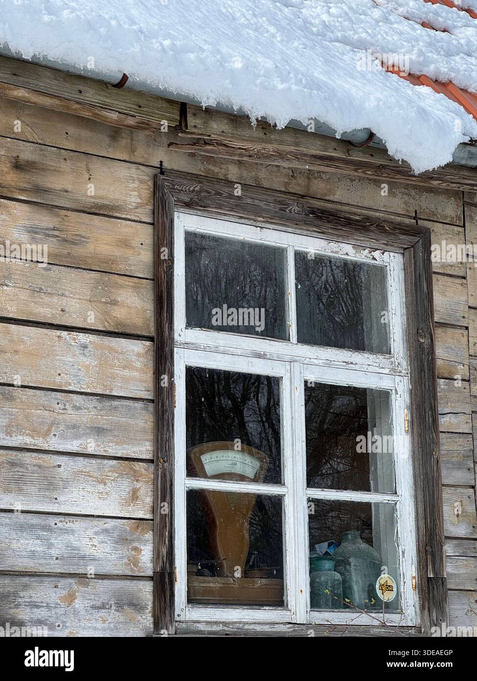 Edificio rustico ricoperto di neve con finestra incorniciata di bianco che riflette il paesaggio invernale e la scala d'epoca all'interno - Immagine stock catturata con smartphone
