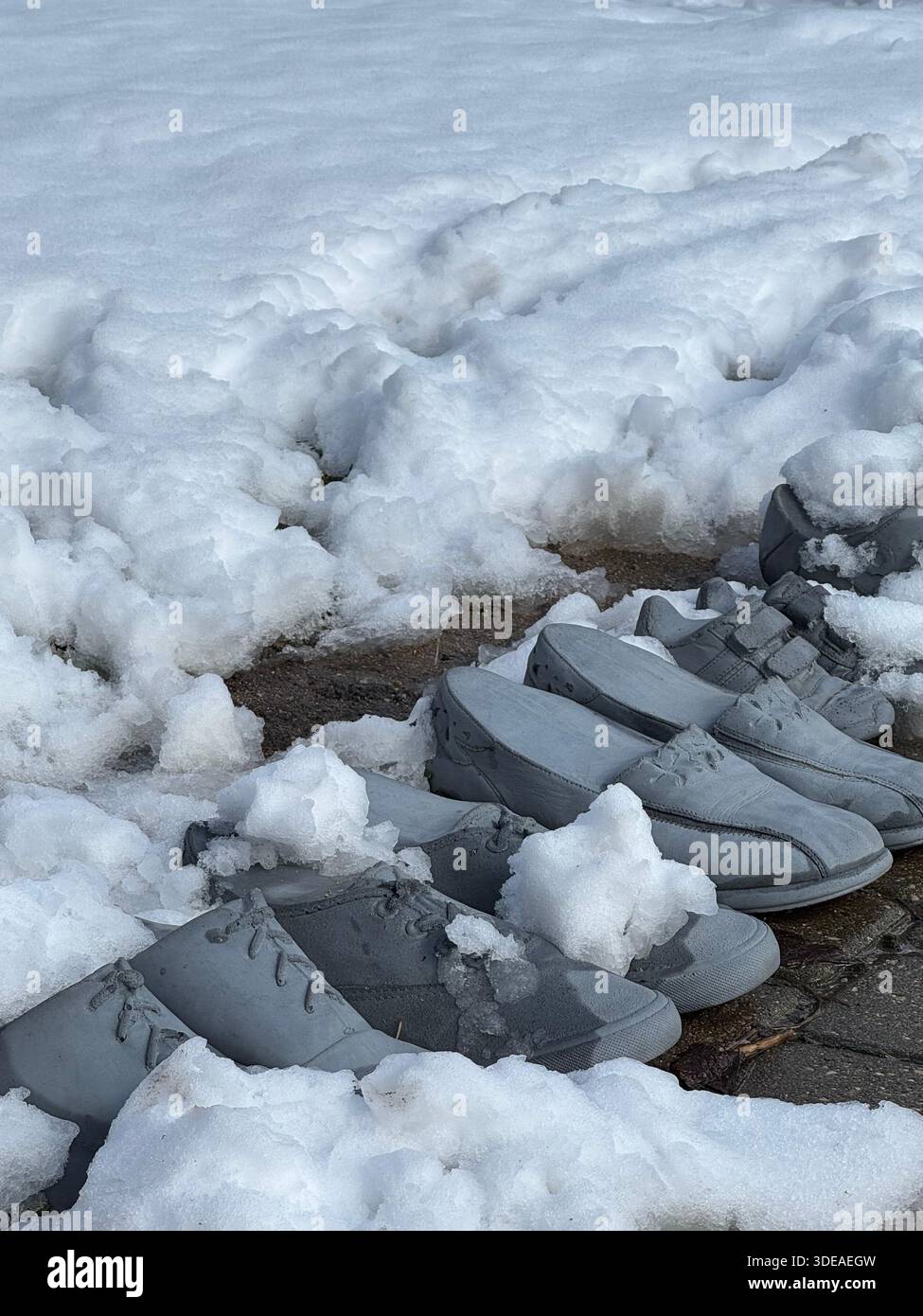 Scarpe congelate parzialmente sepolte nella neve su una superficie pavimentata, evocando abbandono e difficoltà invernali - Immagine stock catturata con smartphone