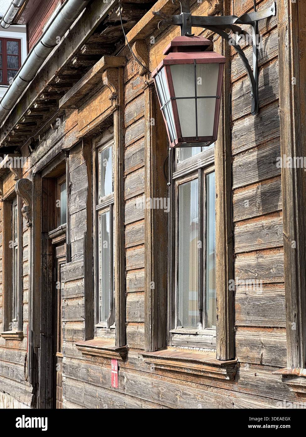 Edificio in legno intempestivo con finestre decorative e lanterna vintage montata sulla facciata - Immagine stock catturata con smartphone