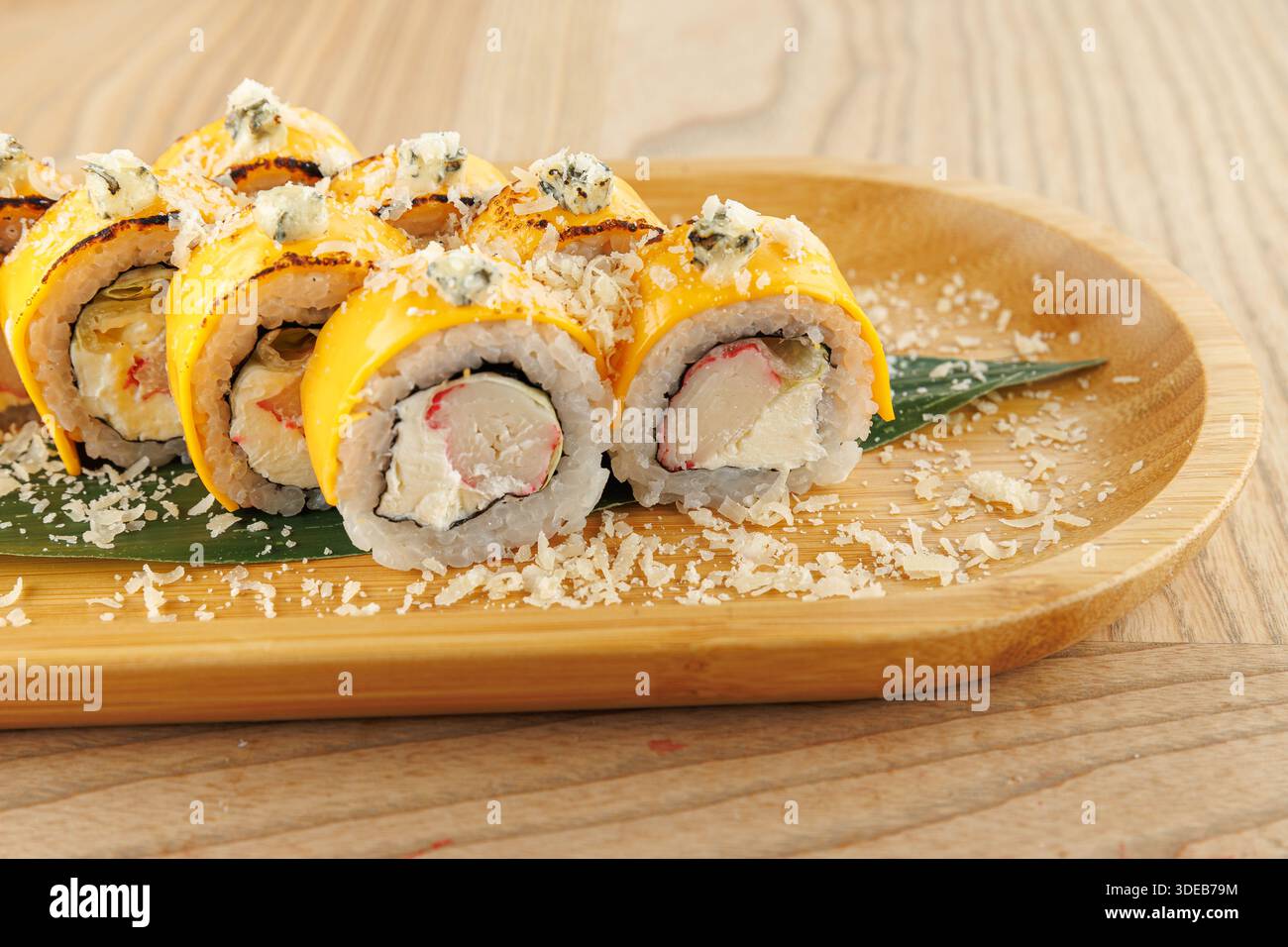 Un piatto propone sushi roll preparati in modo ordinato. I panini sono ricoperti di formaggio grattugiato e posti su una foglia verde, evidenziandone i colori Foto Stock