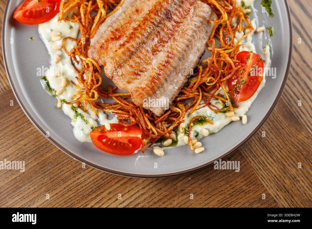 I piatti mostrano pesce alla griglia servito su un letto di patate fritte croccanti, accompagnato da fette di pomodoro fresco e un filo di salsa, il tutto su un decorativo Foto Stock