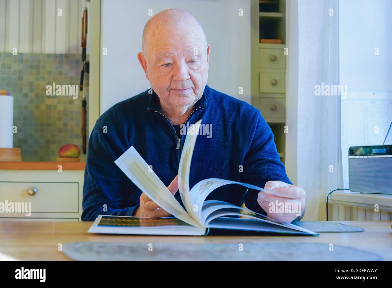 Saggezza quotidiana e riflessione calma con un uomo più anziano che gira pagine di un libro in casa, espressione premurosa e ritmo lento che mettono in risalto il cur per tutta la vita Foto Stock