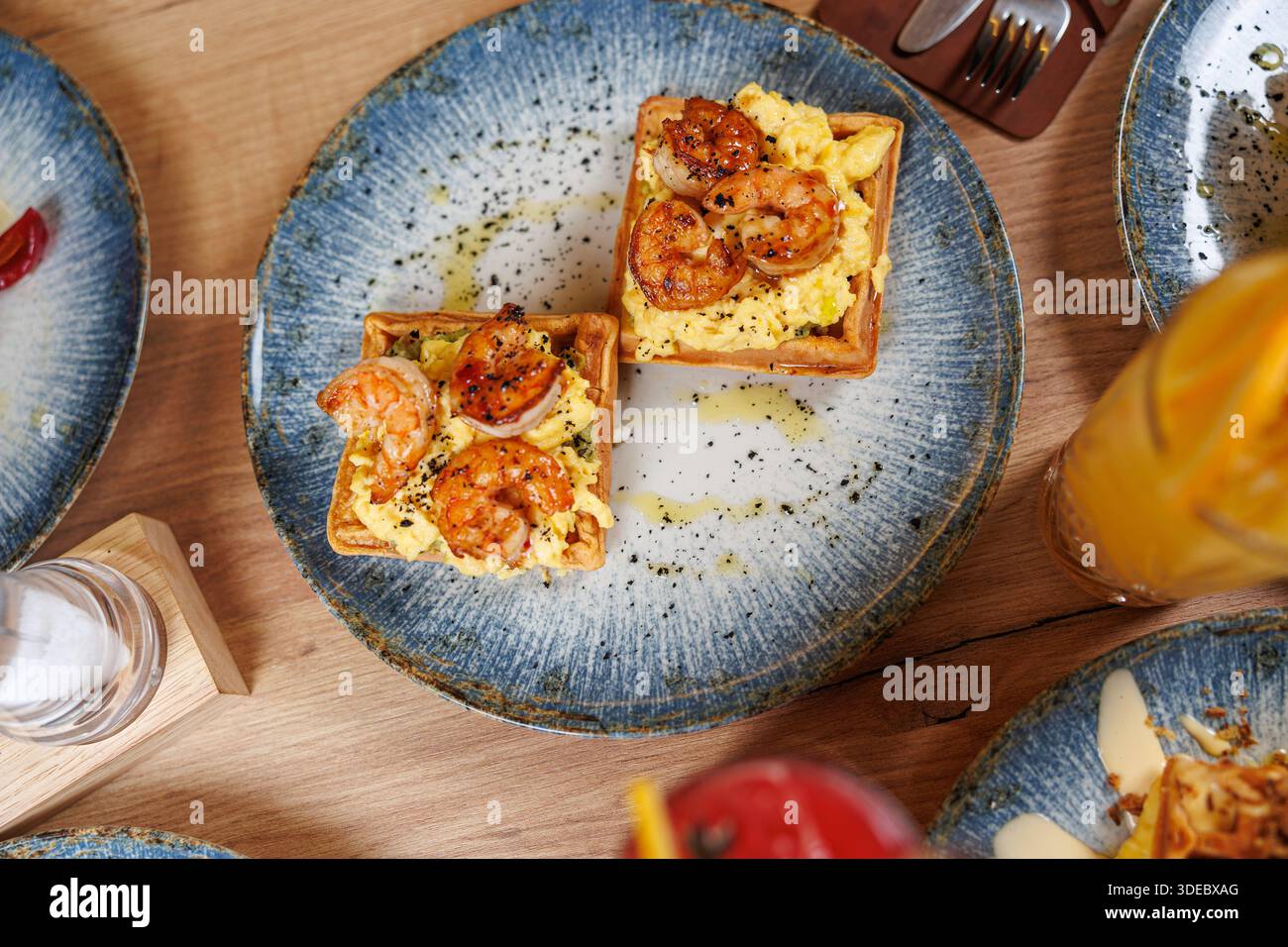 Il brunch viene servito con gamberi sopra le uova strapazzate piegate all'interno delle tazze per waffle. Due piatti propongono questo piatto in un ambiente caldo e invitante. Foto Stock