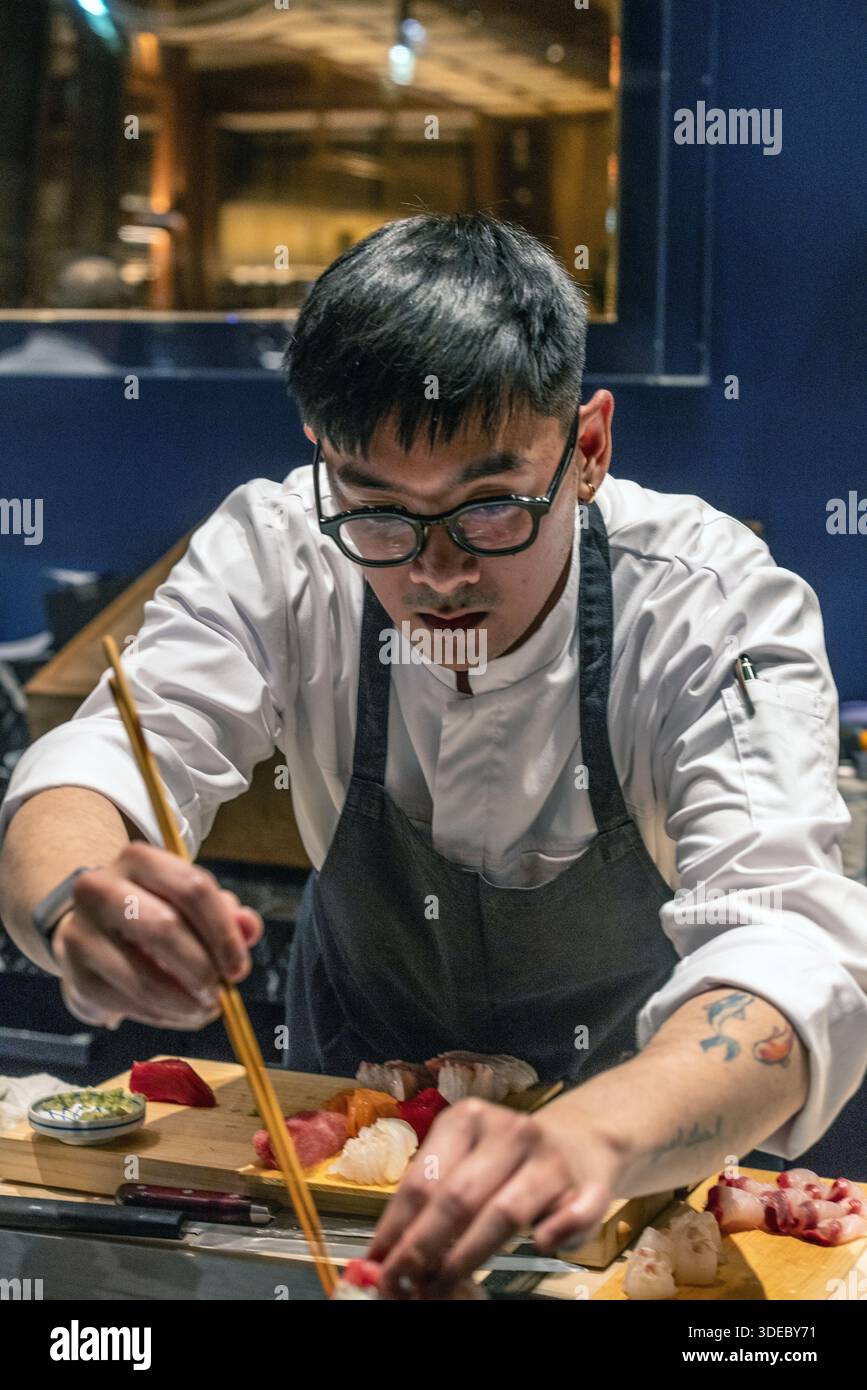 Lo chef sushi prepara meticolosamente sashimi freschi al sushi bar in un esclusivo ristorante giapponese. Foto Stock