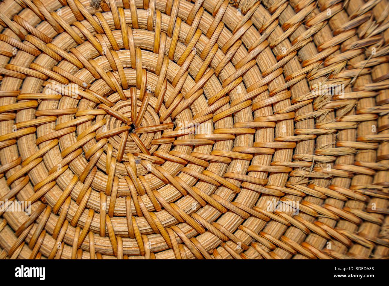 Primo piano della trama circolare in rattan intrecciato con motivo a spirale, che mostra fibre marroni naturali e dettagli artigianali per lo sfondo. Foto Stock