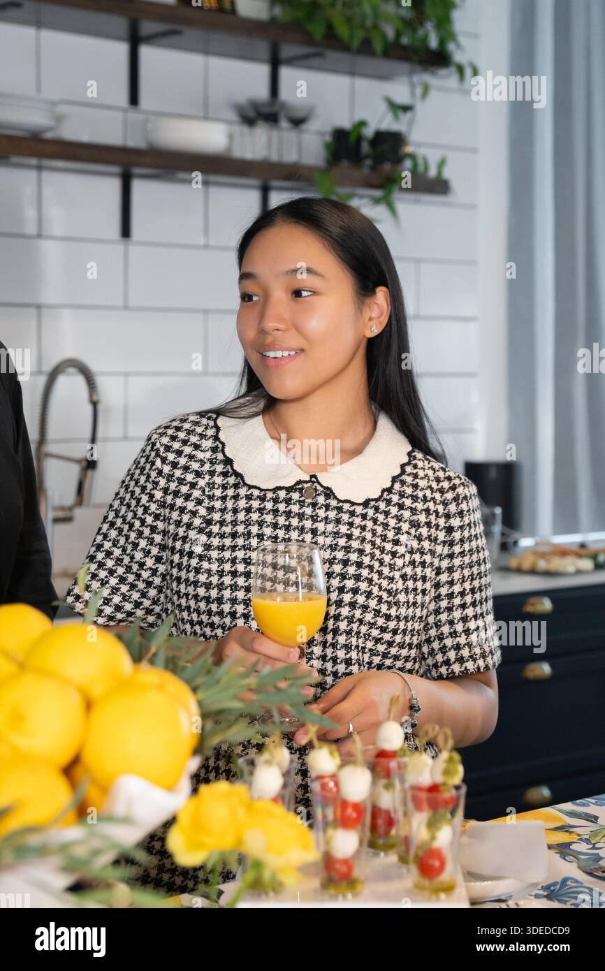 Ragazza asiatica vestita in abito a quadri, in piedi e sorridente al tavolo fisso per la cena di festa Foto Stock