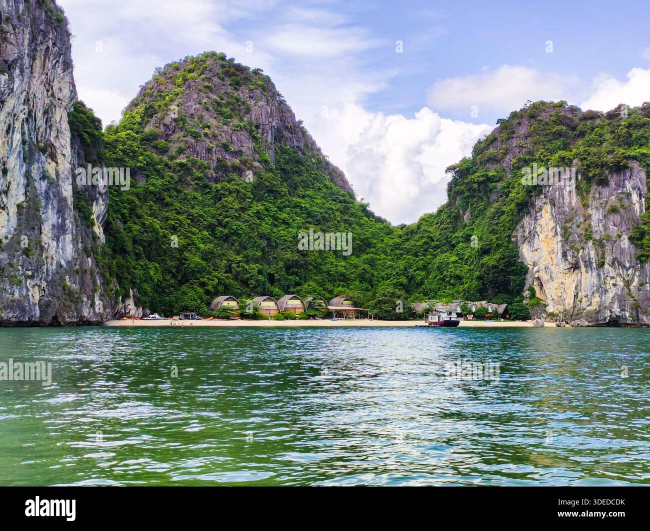 Resort sulla spiaggia appartato con bungalow nella Baia di ha Long, Vietnam. Iconiche formazioni carsiche di pietra calcarea e acqua color smeraldo sotto un cielo blu. Foto Stock