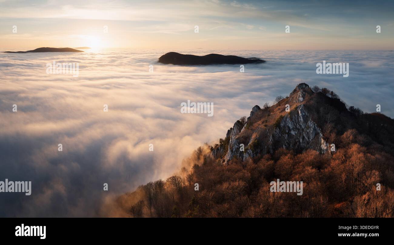 Tramonto con nuvole, raggi del sole e valli nebbiose con foresta, montagne e paesaggi naturali di picco. Foto Stock