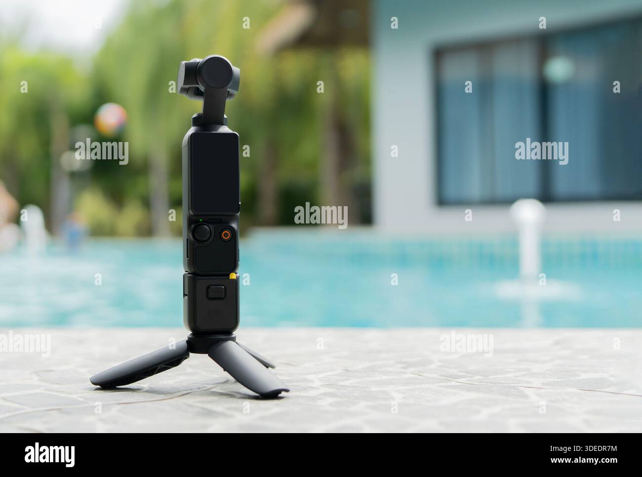 Action camera piccola e treppiede sul pavimento vicino a uno sfondo della piscina con spazio per le copie. Action camera per foto e video. Foto Stock