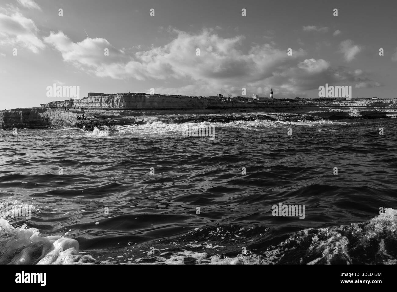 Mare bianco e nero di costa rocciosa frastagliata con onde che si infrangono contro la costa, enfatizzando il contrasto, le texture e la natura selvaggia della costa in un tempo Foto Stock