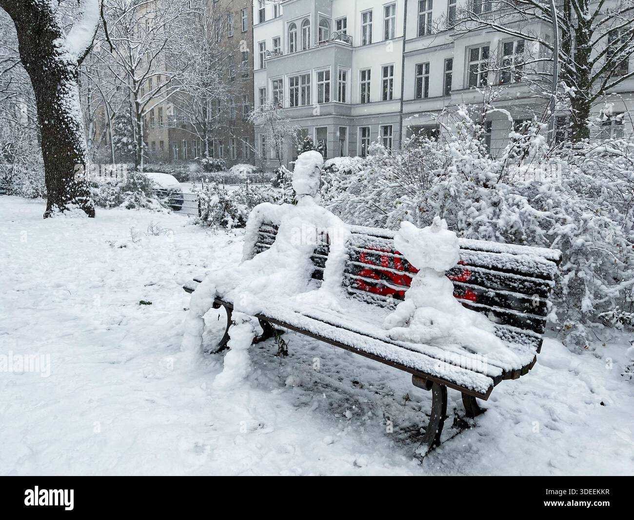 Pupazzo di neve e cane da neve seduti su una panchina a Berlin Kreuzberg in una giornata invernale nevosa al parco Grimmstrasse. Foto Stock