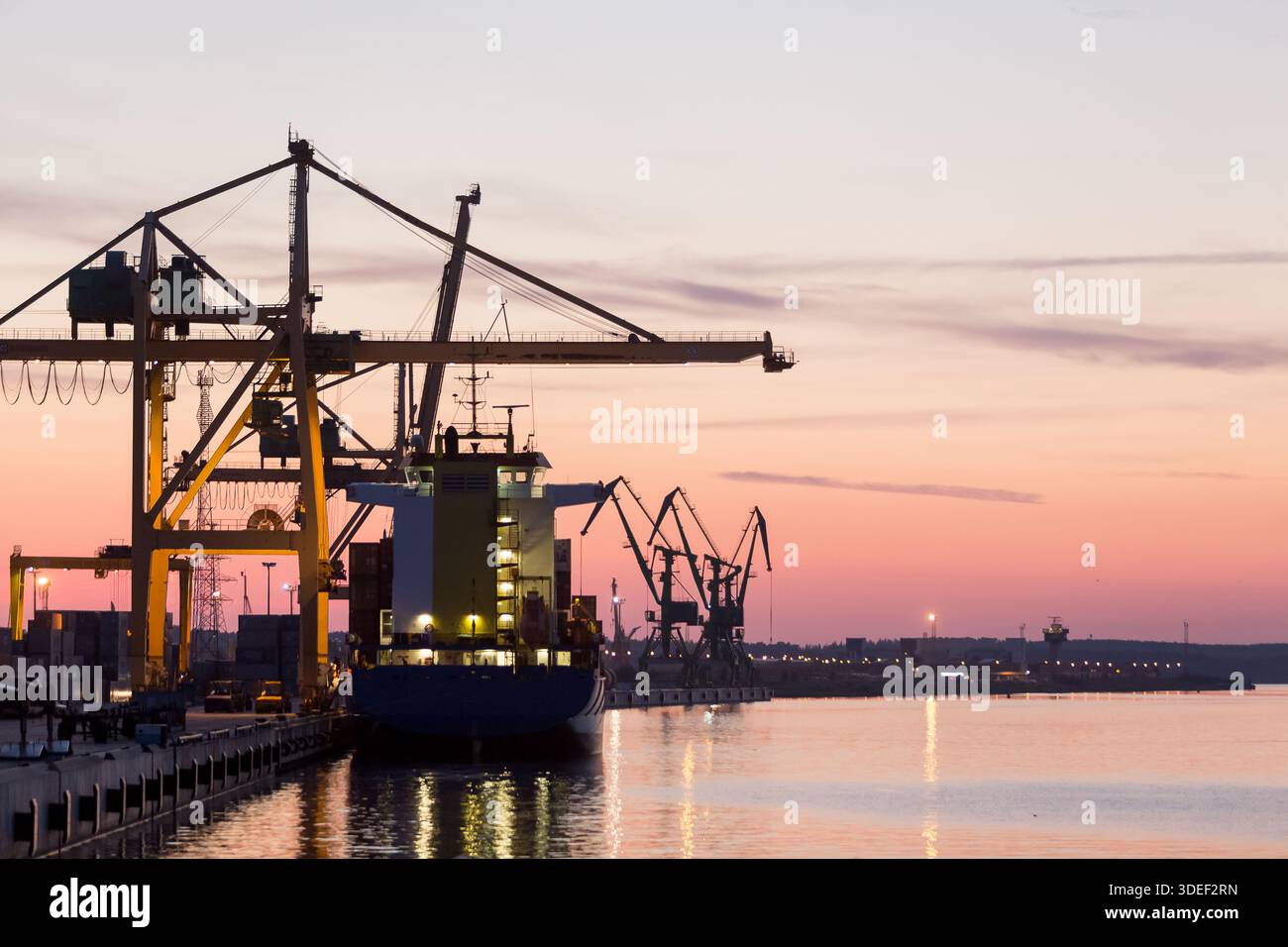 Sagoma di una nave portacontainer ormeggiata accanto alle gru portacontainer nel porto al tramonto, Klaipeda, Lituania Foto Stock