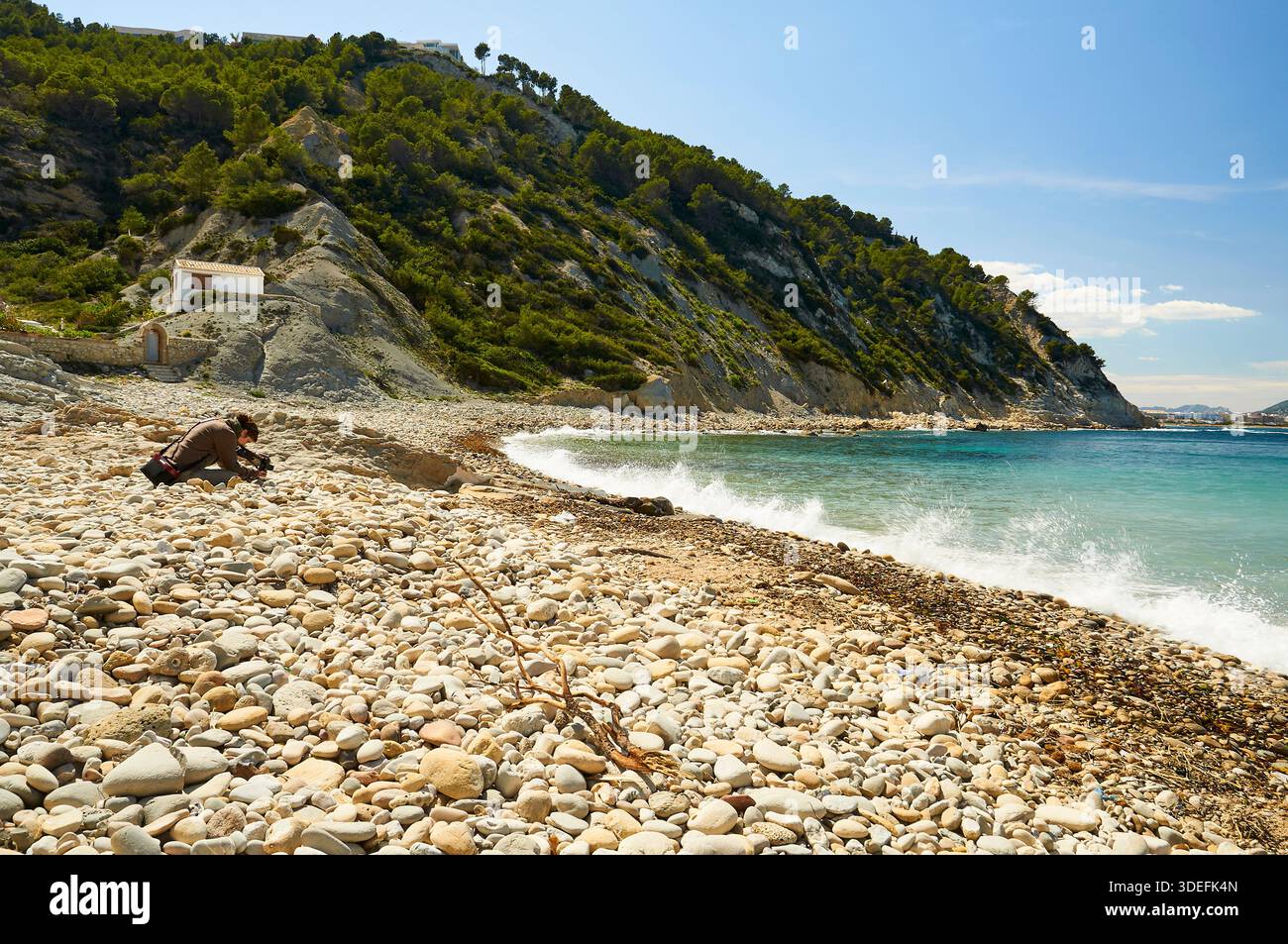 Fotografa donna che fotografa la spiaggia di ciottoli di Cala Sardinera in una giornata soleggiata e limpida (Portichol, Jávea, Marina alta, Alicante, Spagna) Foto Stock